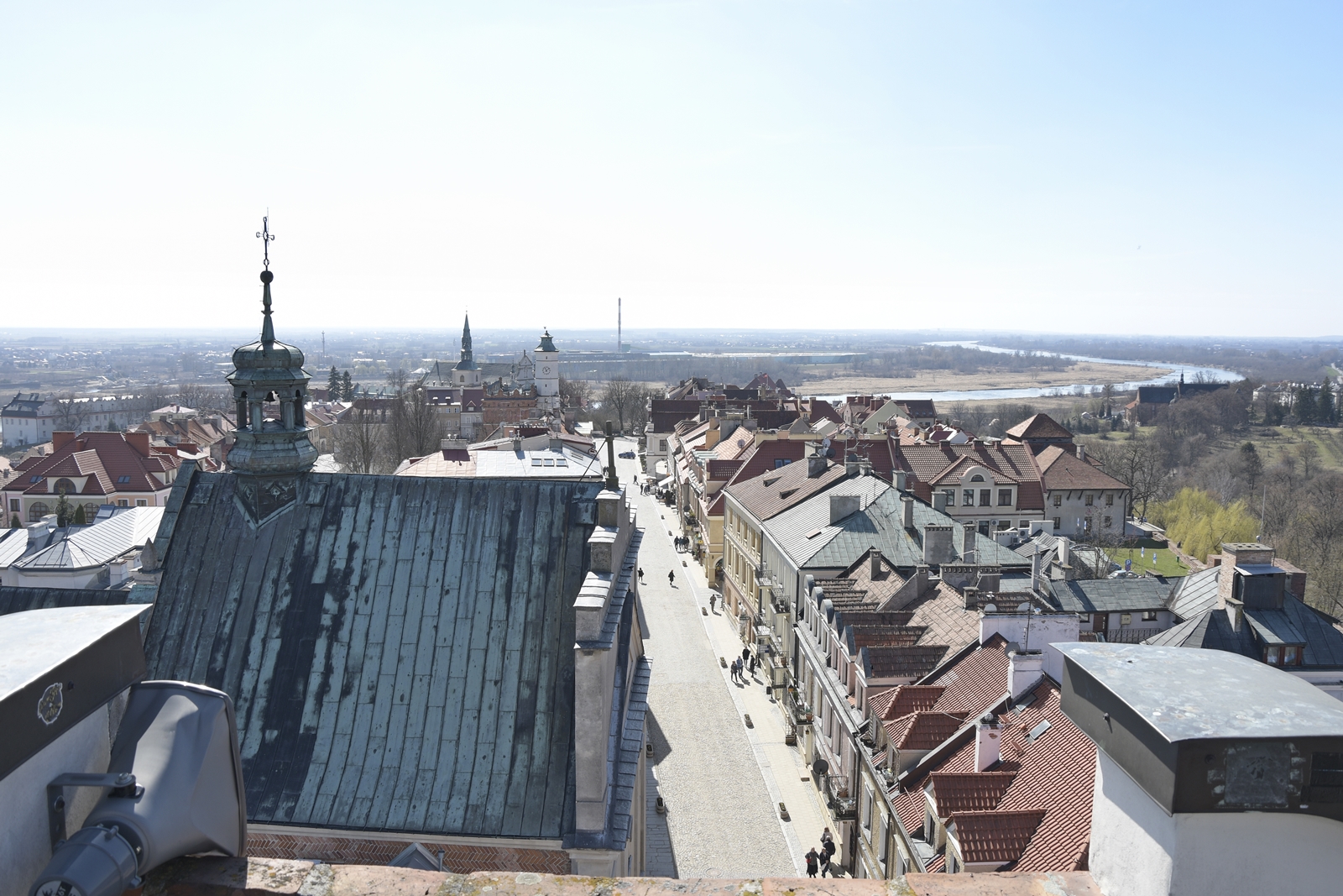 Z tarasu widokowego Sandomierza widać dachy kościoła i kamienic. W oddali widoczna Wisła.