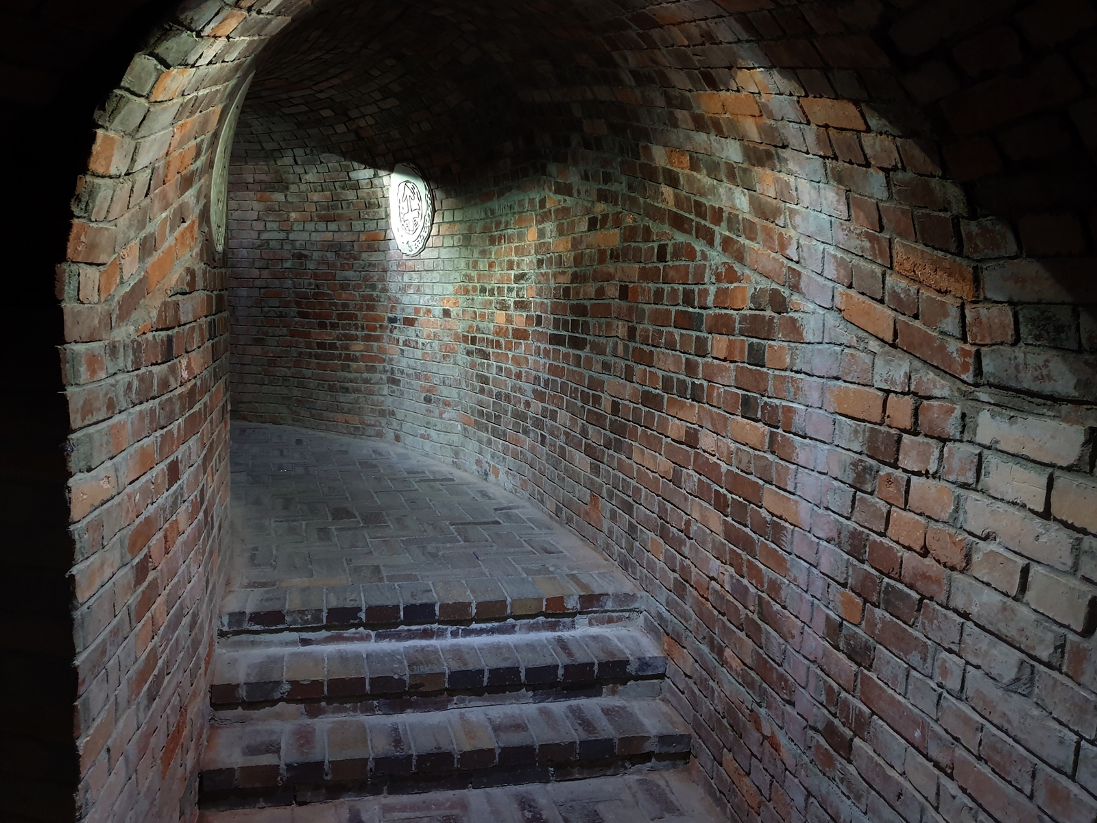 Wnętrze podziemi, ze schodami i ceglastymi ścianami.