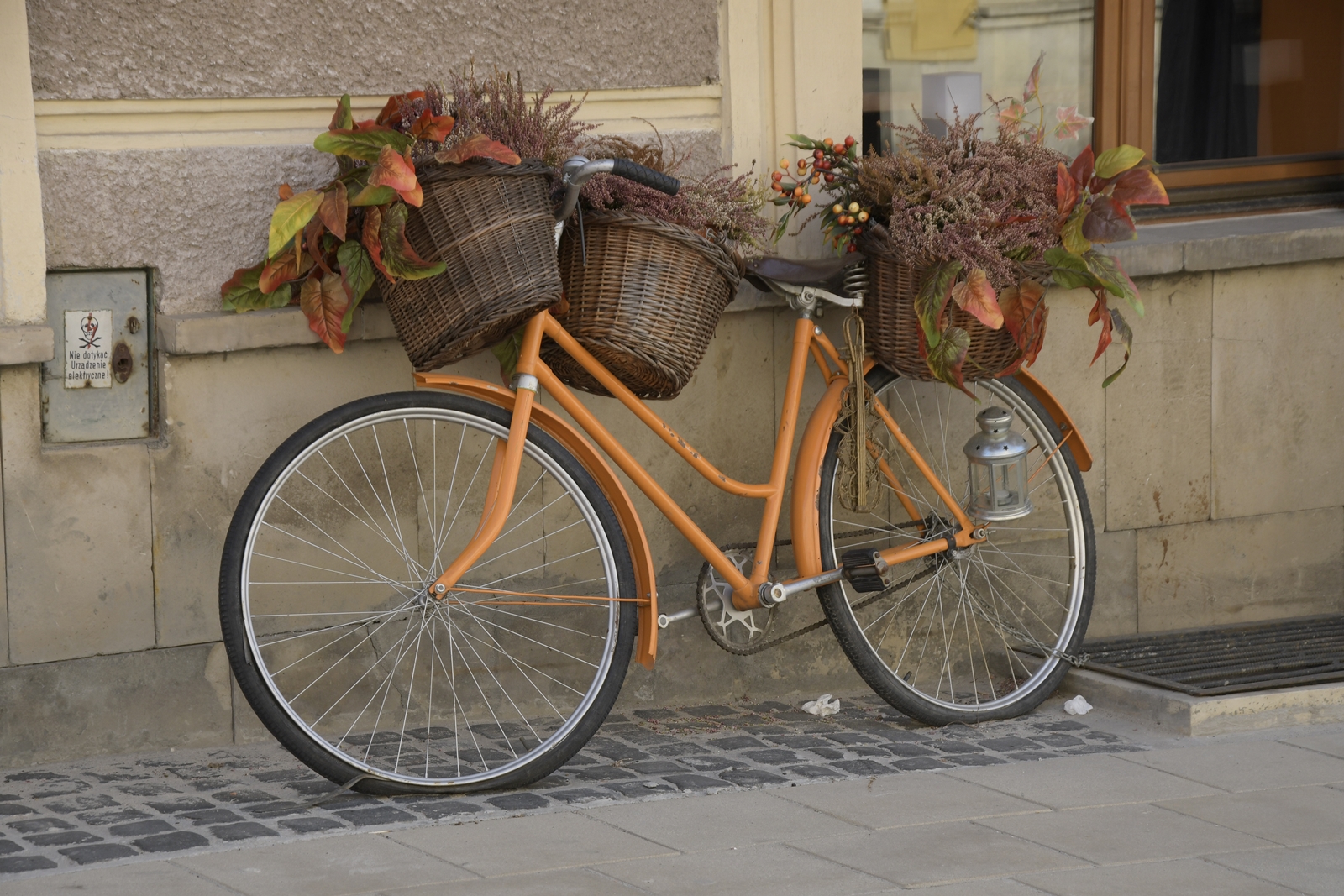 pomarańczowy rower w jesiennej szacie - z wiklinowymi koszykami, wypchanymi kolorowymi liśćmi.