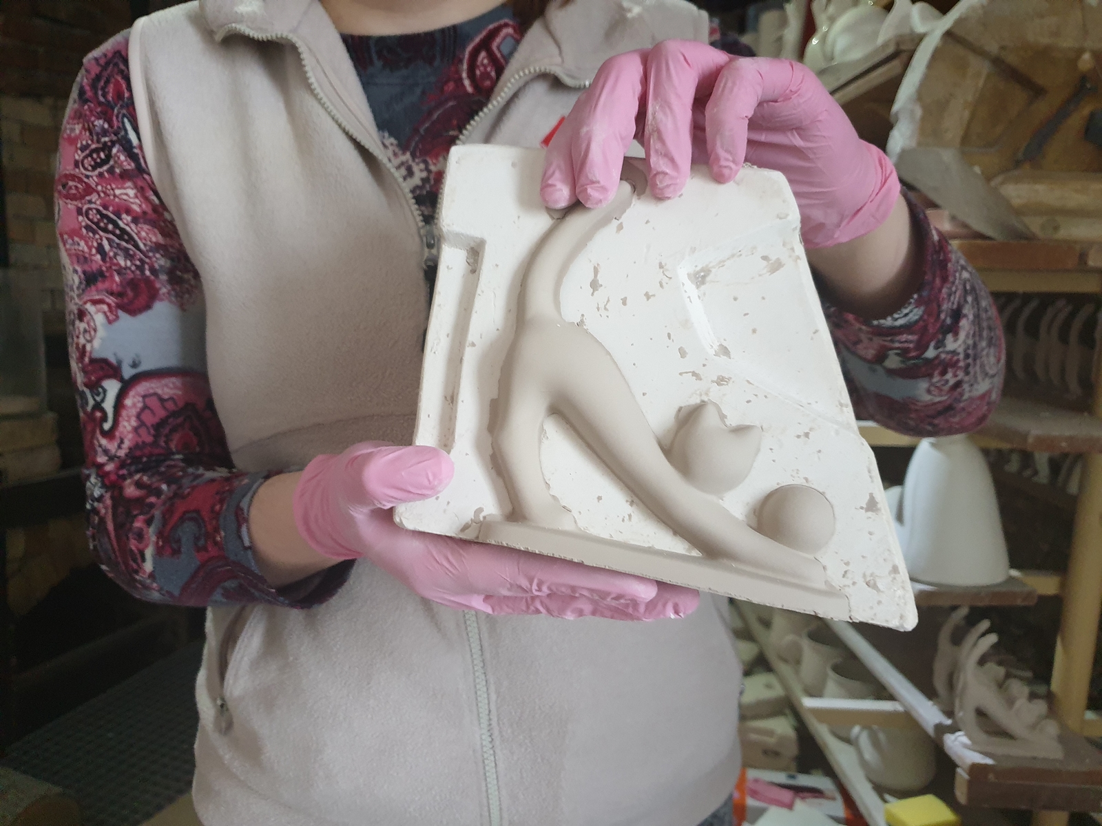 Ręce pracownicy trzymającej figurę kota w formie w Żywym Muzeum Porcelany.