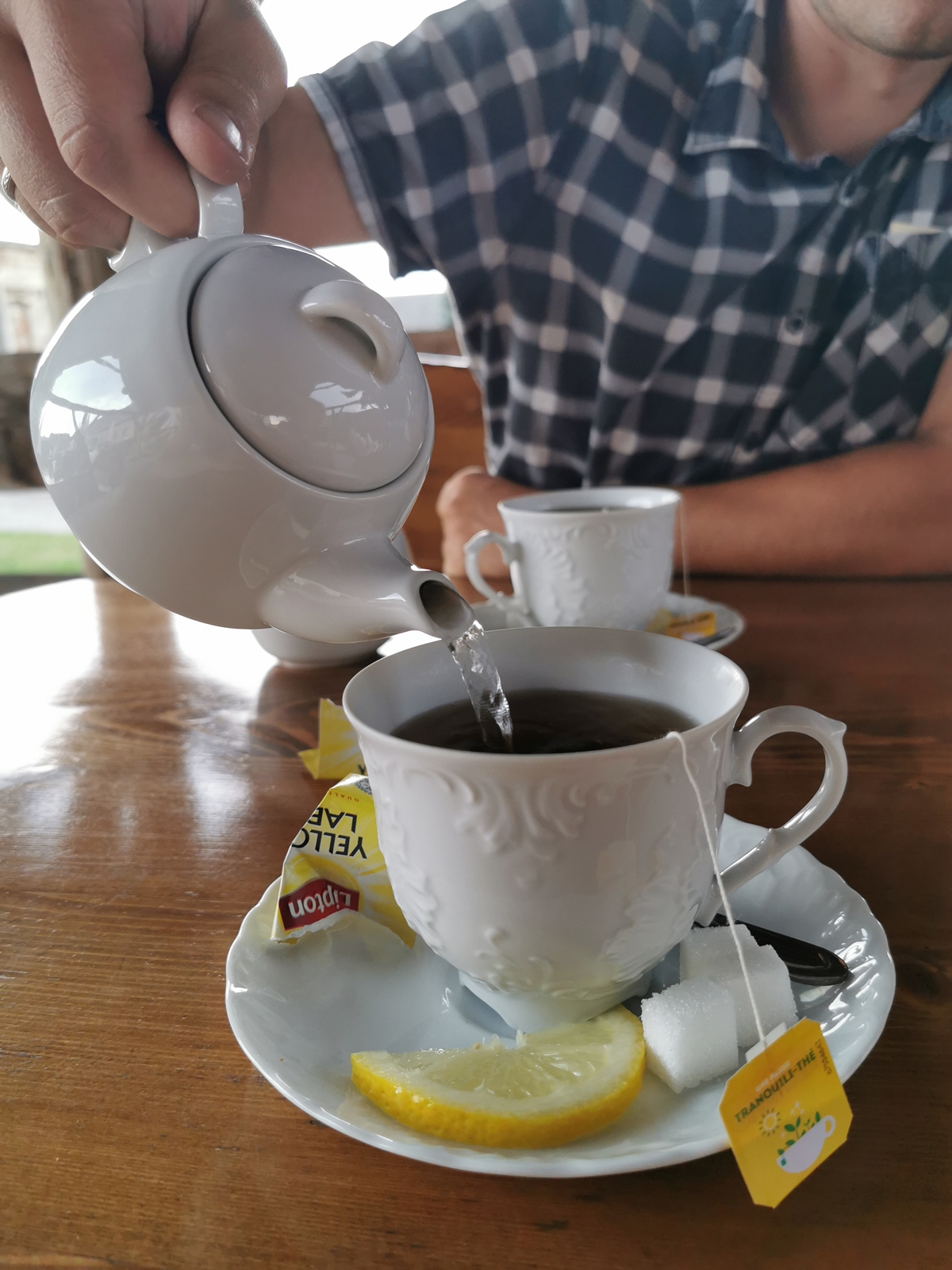 Męska dłoń nalewająca herbatę z imbryczka do filiżanki.