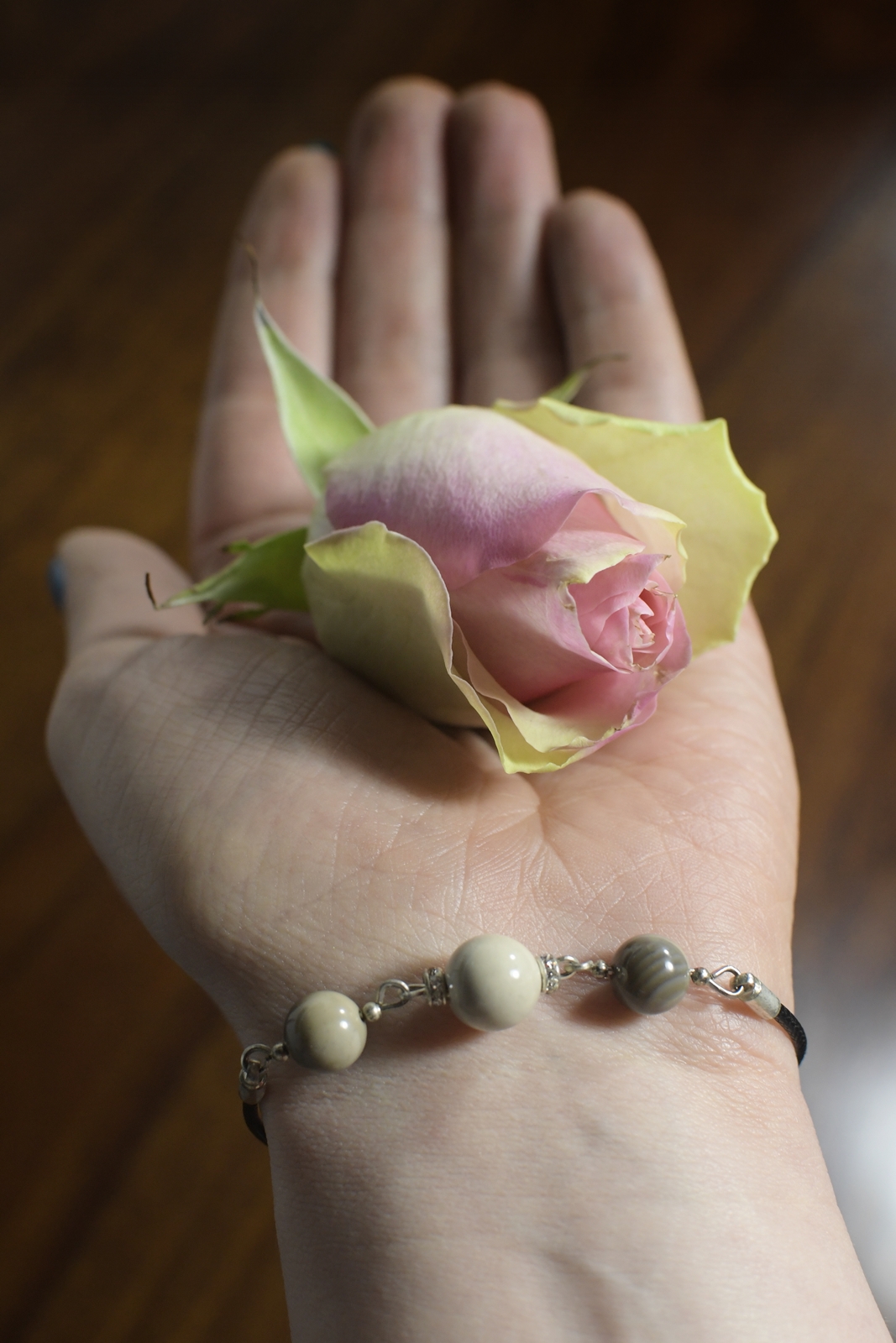 Wyciągnięta dłoń z ułożoną na niej "główką" róży, na nadgarstku biżuteria z krzemienia pasiastego.