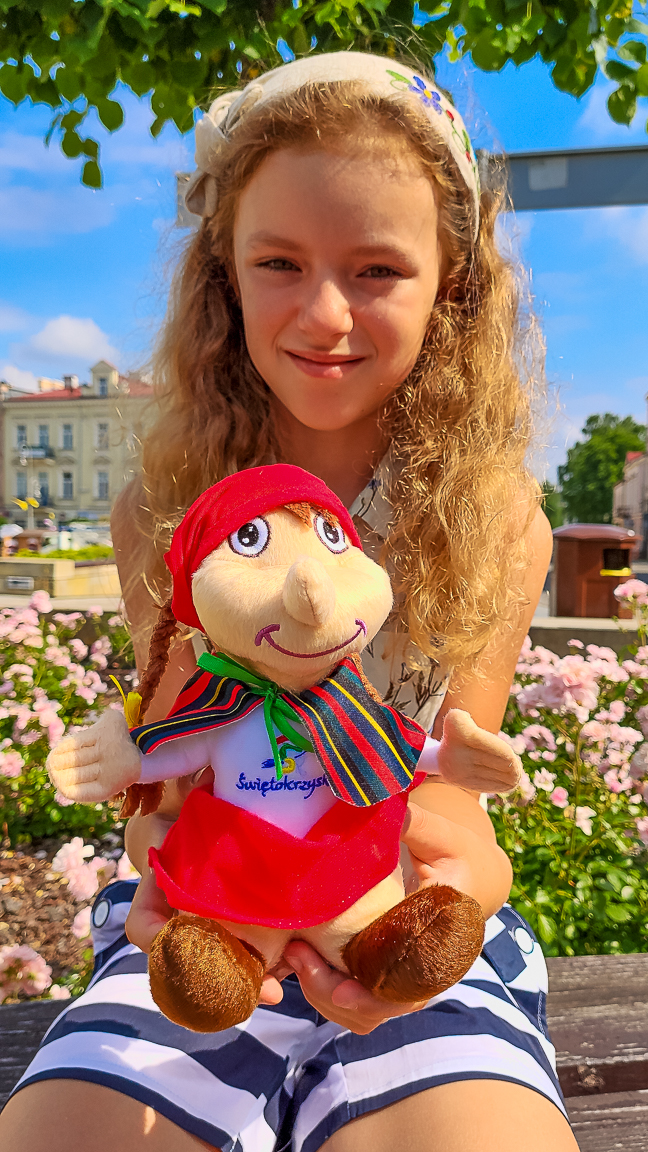 Dziewczynka trzymająca maskotkę świętokrzyskiej Baby Jagi. Czarownica to ciekawa pamiątka ze Świętokrzyskiego.