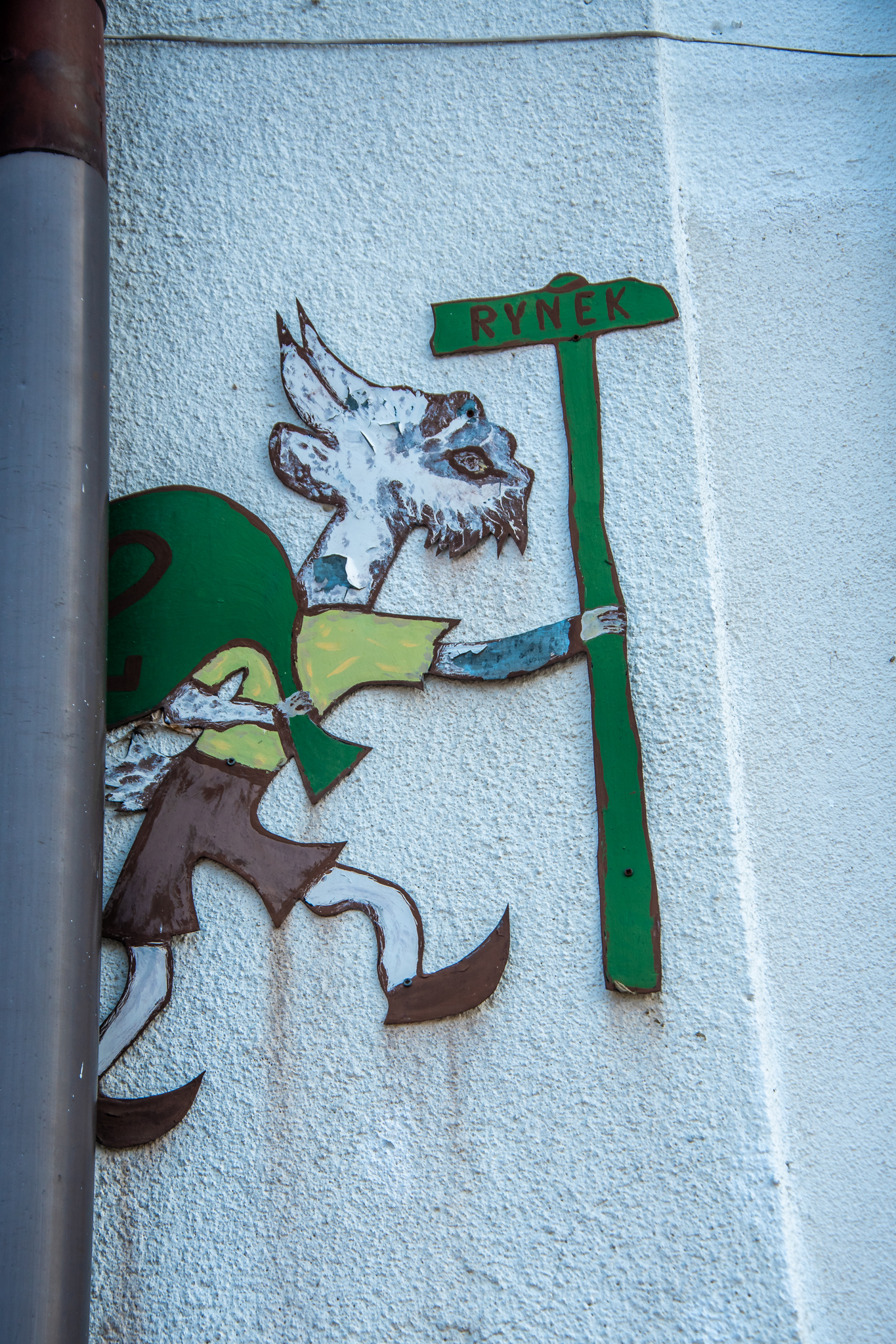 Ręcznie malowany Koziołek Matołek przyklejony do domu z oznaczeniem kierunku Rynku.