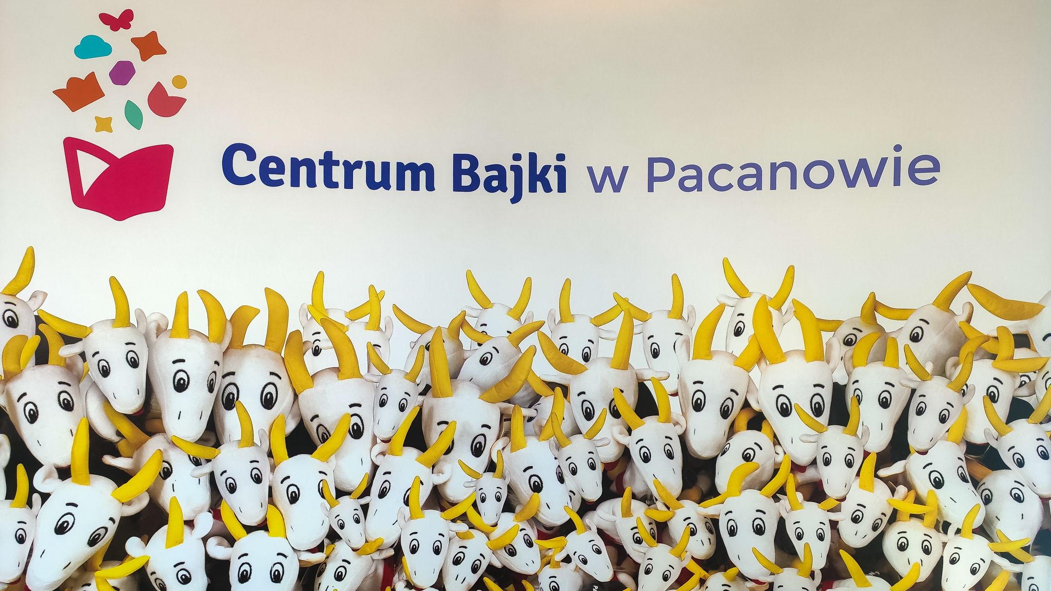 Ścianka do robienie zdjęć - z napisem; "Centrum Bajki w Pacanowie", pod spodem wymalowane maskotki Koziołka Matołka.