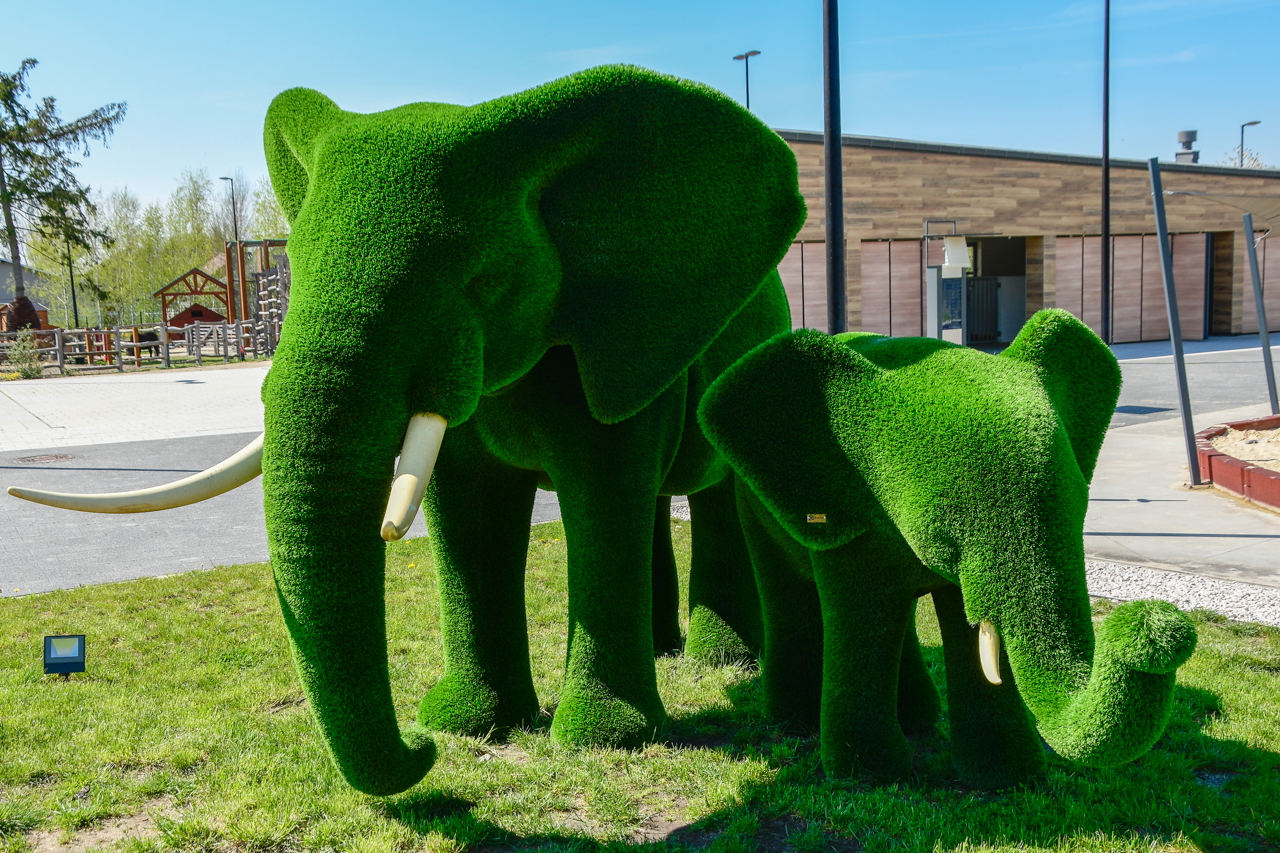 Dwa olbrzymie słonie wykonane z zielonego materiału, przez co wyglądają jak pokryte delikatną trawą.