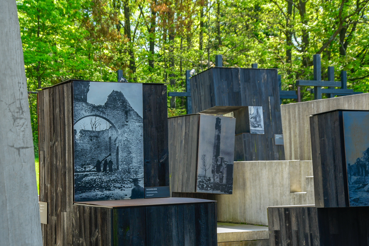 Fragmenty wystawy muzeum Martyrologii Wsi Polskich przedstawiające krzyże i czarno-białe fotografie zrujnowanych wsi.